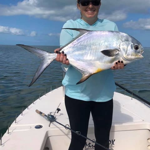 Smiling angler holding a permit on the deck of the skiff