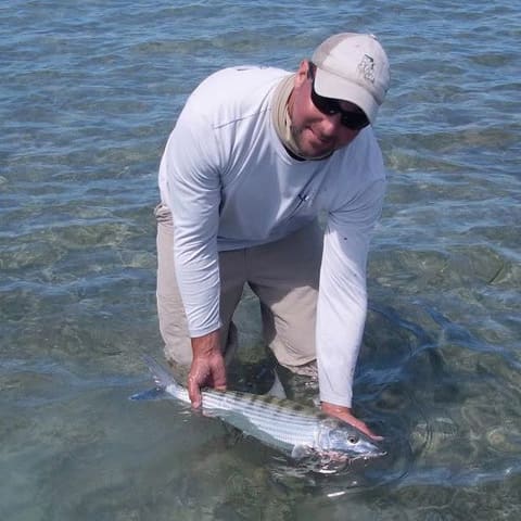 Angler kneeling in shallow water to release a bonefish