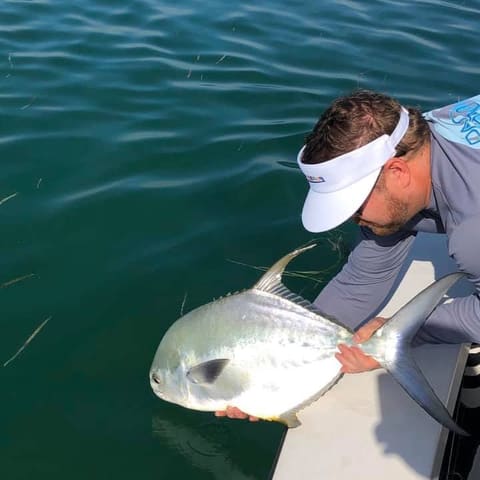 Guide in a white visor releasing a permit at the side of the boat