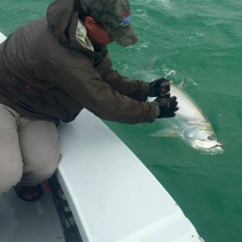 Angler in a camo cap releasing a fish over the side of the skiff