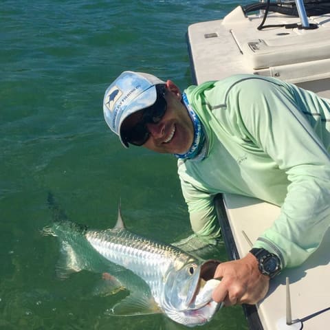 Angler leaning over the gunwale holding a tarpon by the jaw before release