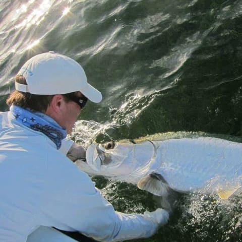 Angler releasing a tarpon beside the skiff in a burst of spray