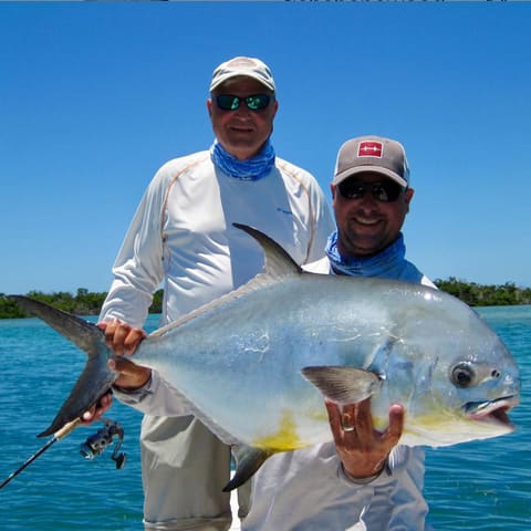 Two anglers hold up a large permit on the flats